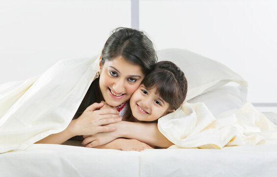 Portrait of mother and daughter covered with a bed sheet 