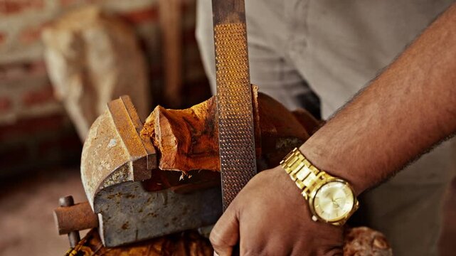 A woodcarver works a piece of timber with a hand file in a village workshop where carvings and tools fill the bench in Sri Lanka. The craft is passed down through generations.
