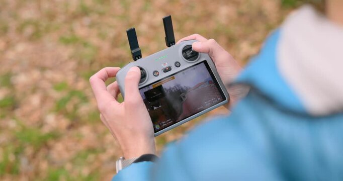 Close-up view of pilot hands holding drone remote controller with display screen operating flight outdoors
