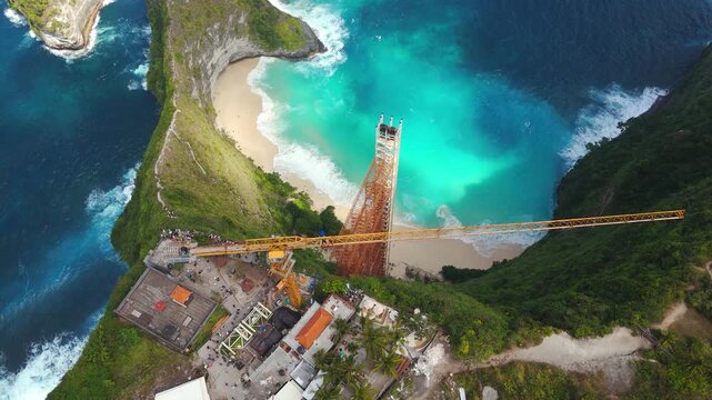 Glass elevator ordered for demolition scars Kelingking Beach's protected cliff, revealed in an upward drone tilt.