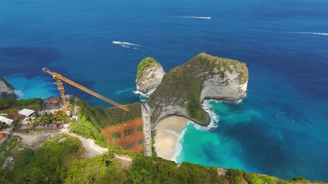 Unfinished elevator structure rises beside Kelingking Beach's T Rex cliff in a smooth right-orbit drone shot.