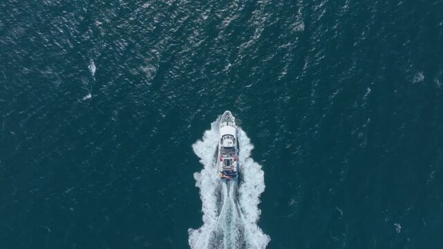Passenger ferry powers through deep blue water leaving a white wake in this overhead drone flyover shot.