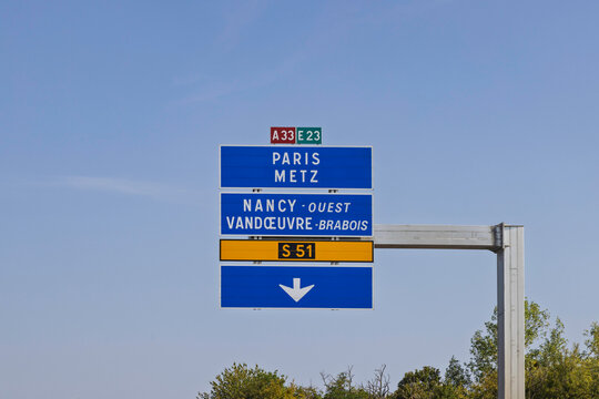 Nancy, France. French highway directional road sign overhead showing routes to Paris, Metz, and Nancy-Ouest under clear blue sky.