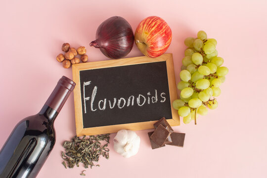 Products containing beneficial flavonoids. Grapes, onions, garlic, chocolate, tea &mdash; close‑up on a light background, and the text &ldquo;flavonoids&rdquo; on a dark board.