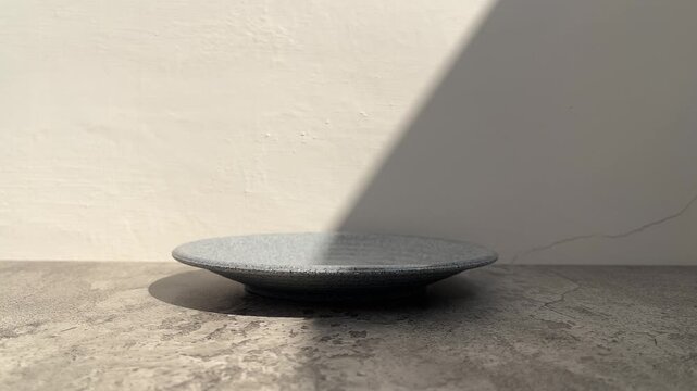 side view of empty grey plate with shadows. gray cement table. white wall. copy space, empty, free, negative, text, design. black, dark. line, lines. sunlight, sunrise, sunshine. product. close up.