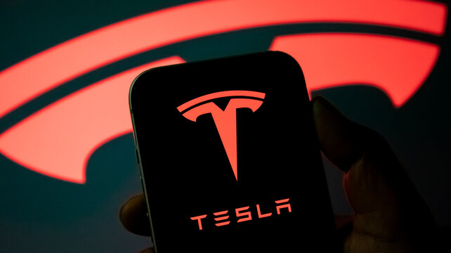 Smartphone holding glowing red tesla logo icon for electric vehicle technology automotive marketing and corporate news reporting.