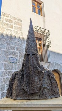 The sculpture depicts a Nazareno (penitent) of the Spanish Holy Week (Semana Santa), wearing a traditional pointed hood called a capirote.