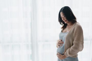 Fototapeta premium Asian pregnant woman touching her belly at home