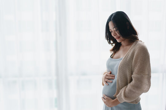 Asian pregnant woman touching her belly at home