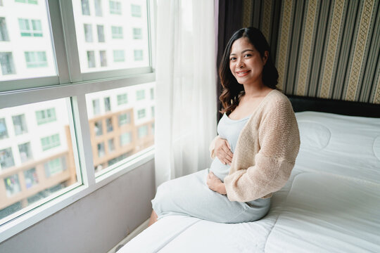 Asian pregnant woman touching her belly at home
