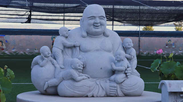 Smiling Hotei Buddha Statue with Happy Children Sculptures in a Peaceful Asian Temple Garden Setting