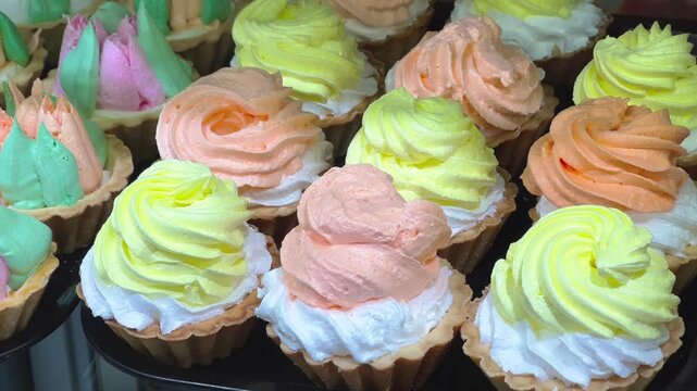 Fresh sweet mini tartlets with colorful whipped cream rosettes displayed in a bakery shop, food industry and restaurant, sweet dessert indulgence.