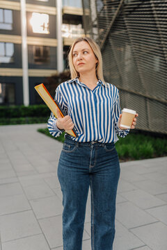 Businesswoman walking outdoors holding folder and coffee