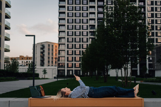 Woman relaxing on park bench checking phone