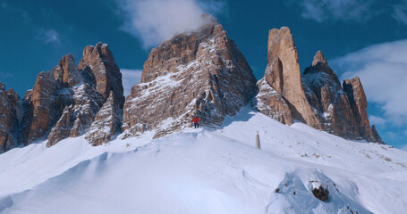 Obraz premium Ski mountaineer crossing a snowy ridge in the Dolomites with dramatic alpine peaks and blue sky in the background, capturing winter adventure and breathtaking mountain landscape.