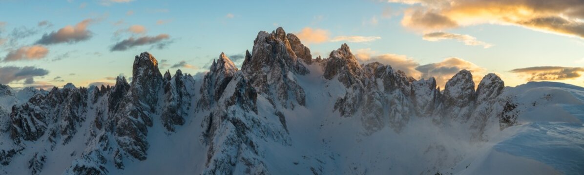 Panoramic winter view of the Dolomites at sunset with dramatic rocky peaks and snow covered ridges under colorful clouds, showcasing majestic alpine scenery in high resolution.