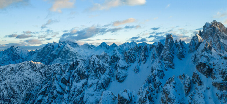 Panoramic winter view of the Dolomites at sunset with dramatic rocky peaks and snow covered ridges under colorful clouds, showcasing majestic alpine scenery in high resolution.