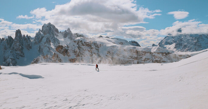 Ski mountaineer crossing a snowy ridge in the Dolomites with dramatic alpine peaks and blue sky in the background, capturing winter adventure and breathtaking mountain landscape.