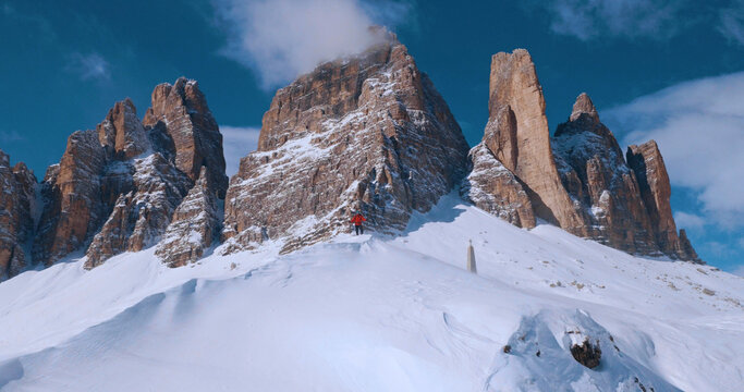 Ski mountaineer crossing a snowy ridge in the Dolomites with dramatic alpine peaks and blue sky in the background, capturing winter adventure and breathtaking mountain landscape.