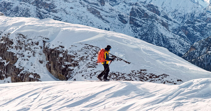 Ski mountaineer crossing a snowy ridge in the Dolomites with dramatic alpine peaks and blue sky in the background, capturing winter adventure and breathtaking mountain landscape.
