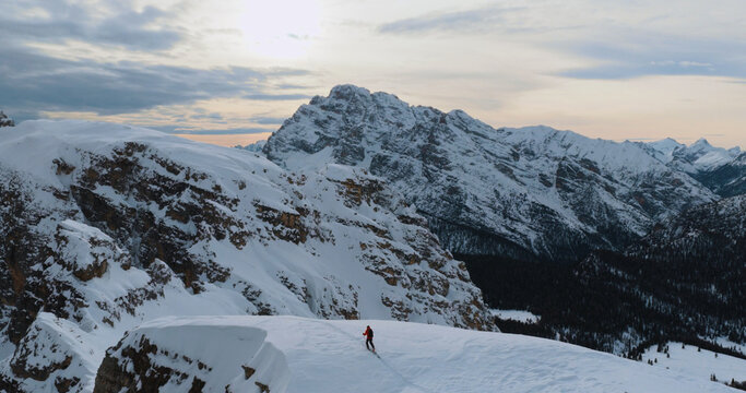 Ski mountaineer crossing a snowy ridge in the Dolomites with dramatic alpine peaks and blue sky in the background, capturing winter adventure and breathtaking mountain landscape.