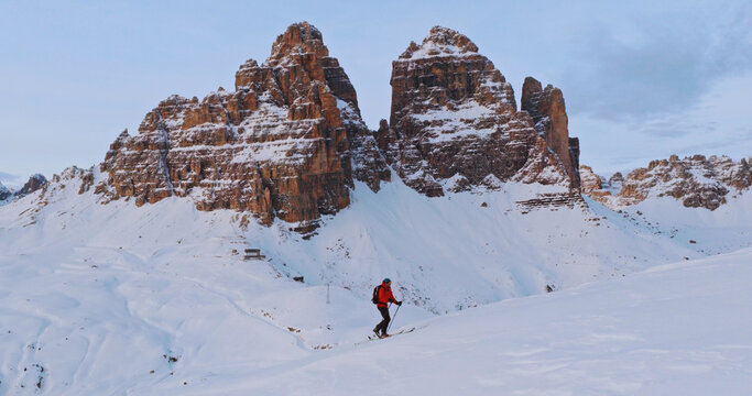 Ski mountaineer crossing a snowy ridge in the Dolomites with dramatic alpine peaks and blue sky in the background, capturing winter adventure and breathtaking mountain landscape.