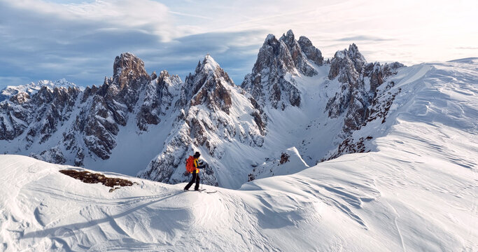 Ski mountaineer crossing a snowy ridge in the Dolomites with dramatic alpine peaks and blue sky in the background, capturing winter adventure and breathtaking mountain landscape.