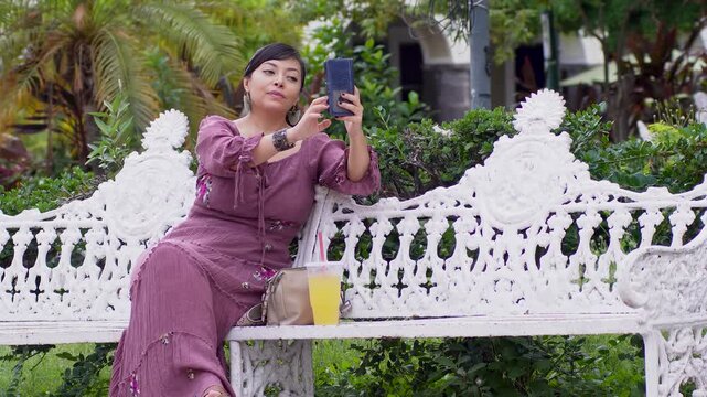 Mexican Woman Taking Selfies on a Park Bench with Her Cell Phone