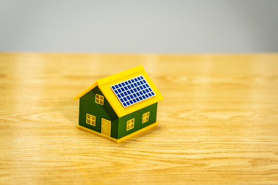 Small green house model with solar panel on a wooden table, symbolizing clean energy, home savings, and eco friendly living