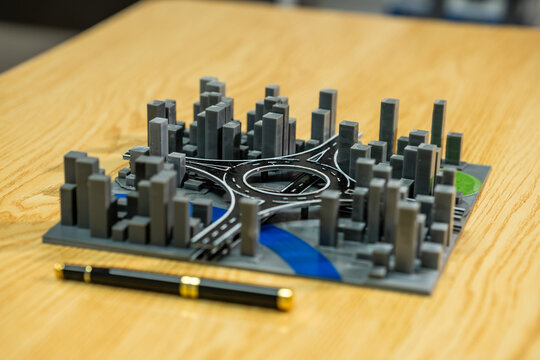 Miniature city model with highway interchange on a wooden table next to a pen