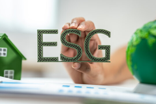 Hand holding esg letters with a green house and globe, showing sustainability and responsible business concept.
