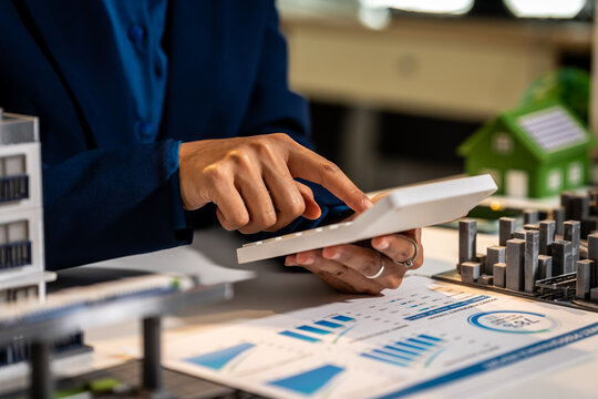 Business person using a calculator on financial charts with small building models, showing real estate planning and investment analysis