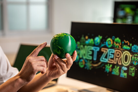 Hands holding a small green globe with a net zero screen in the background, showing a clean energy and sustainability concept