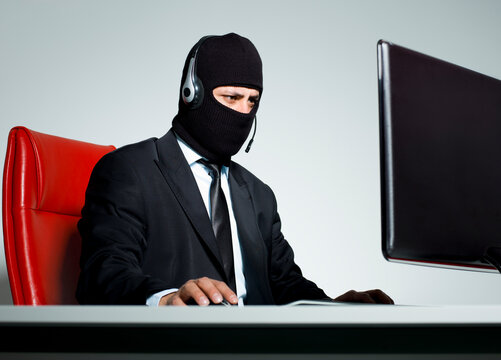 Masked businessman in suit wearing headset working on computer call center fraud concept isolated on white background.