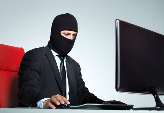 Businessman wearing balaclava working on computer stealing sensitive data cybercrime concept isolated on white background.
