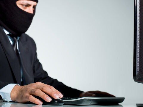 Businessman wearing balaclava working on computer stealing sensitive data cybercrime concept isolated on white background.