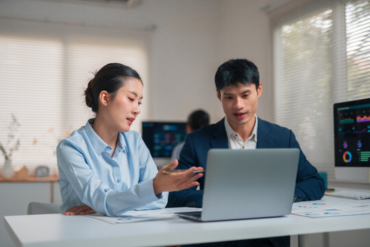 Asian business colleagues collaborating on a laptop in a modern office, analyzing data and discussing financial reports