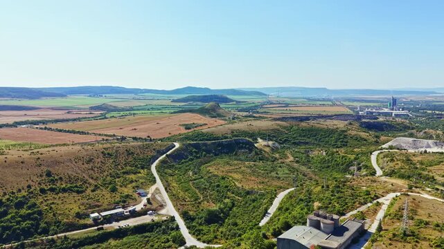A large area shows rolling hills and flat fields. On one side, there is a factory making smoke. Dirt roads wind through the greenery and brown land.