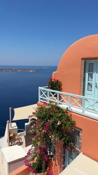 Santorini island, Greece. Colorful architecture with flowers in Oia town. Blue sea and the blue sky at sunny day. Travel and summer vacation concept. Vertical video
