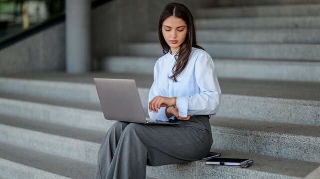 Young woman working on a laptop while sitting on outdoor stairs