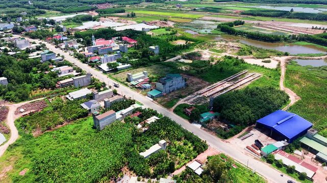 Views of Duc Linh in Lam Dong show houses, roads, and fields. The video captures the landscape and layout of the area in bright daylight. People move around and nature surrounds the location.