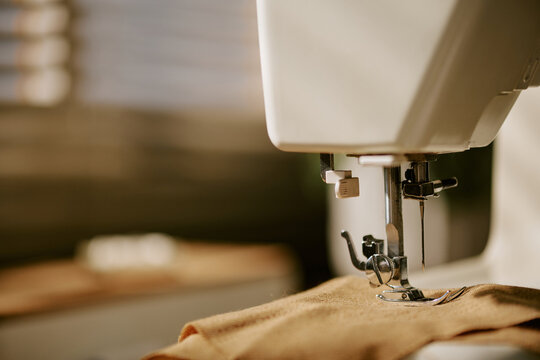 Sewing machine needle stitching brown fabric in workshop, representing textile manufacturing and craft hobby. Image suitable for tailoring school promotions, close up shot