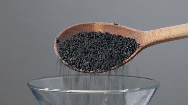 Close up of black cumin seed falling from a wooden spoon