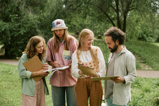Diverse group of young adult artists drawing on clipboards during outdoor master class in park, promoting creative education and community art workshops