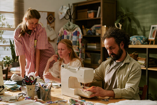 Diverse group of young adult colleagues working in sewing workshop, Caucasian man using sewing machine. Image suitable for small business, craft education, and creative entrepreneurship