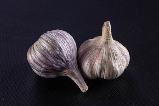 Two garlic bulbs with purple stripes on dark textured background