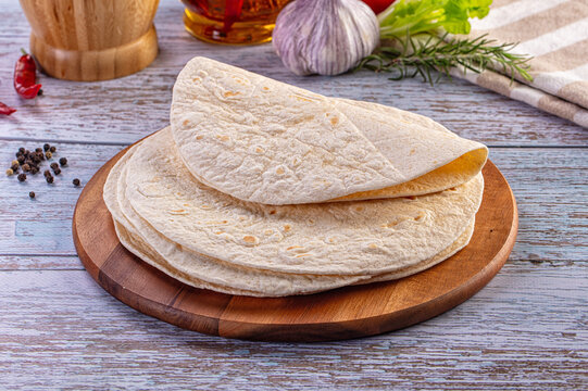 Fresh tortillas or flatbread on a wooden cutting board with rustic ingredients