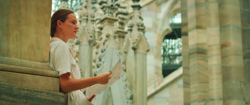 Woman reads a city map while seated among gothic spires on a cathedral rooftop