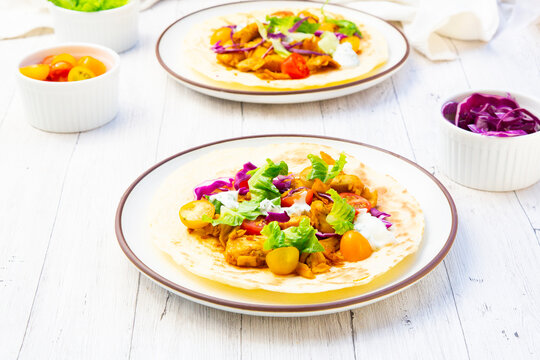 Two plates hold vegetarian gyros wraps on a white wooden table