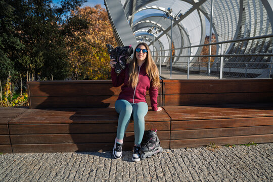 Woman holding rollerblades sitting on park bench